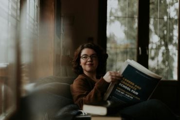 A woman in glasses reading in soft natural light by a window — featured image for an article on plants science says may help protect women's brains from dementia