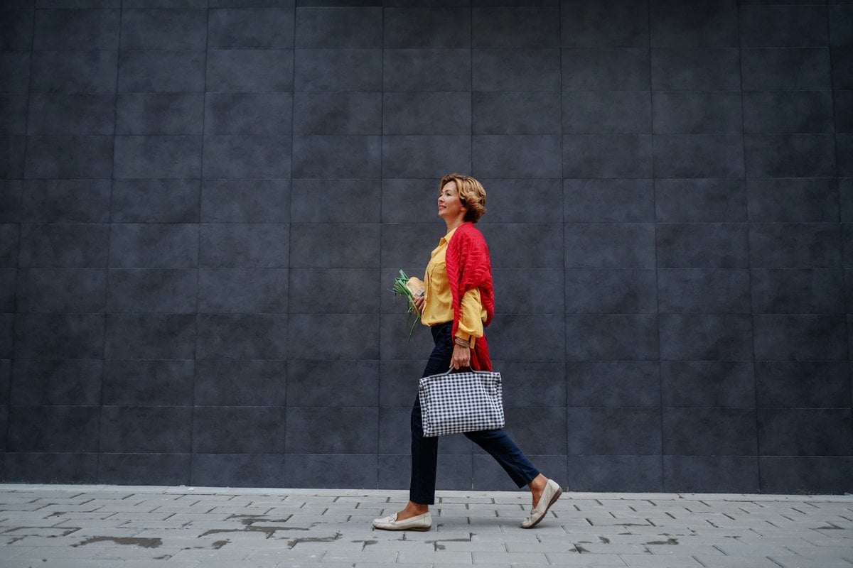 A woman in her sixties walking briskly along a pavement carrying a shopping bag and flowers