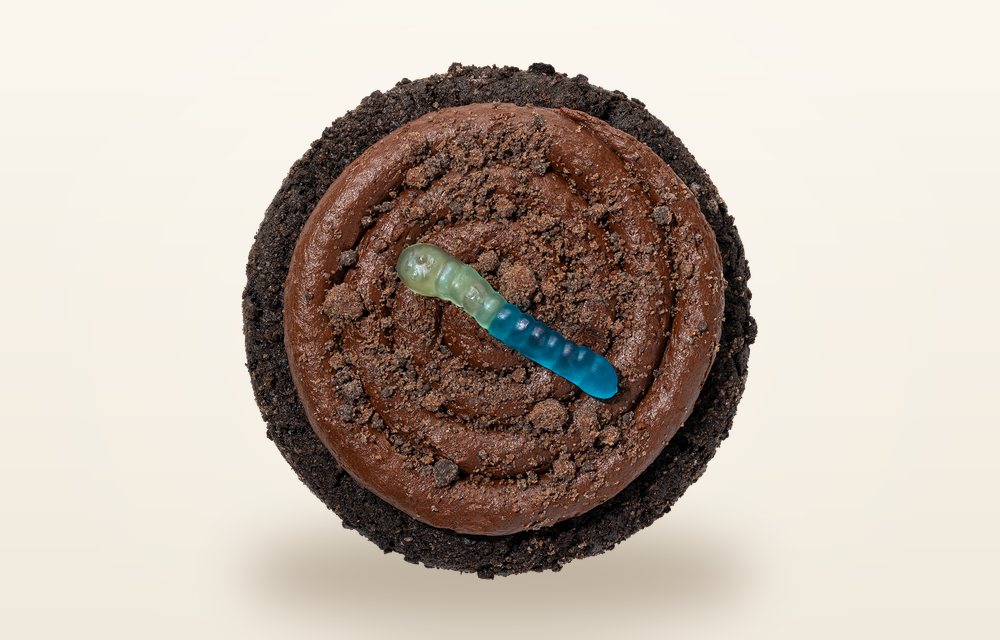 Overhead view of a Crumbl Dirt Cake cookie covered in dark cookie crumbs with a single gummy worm on top