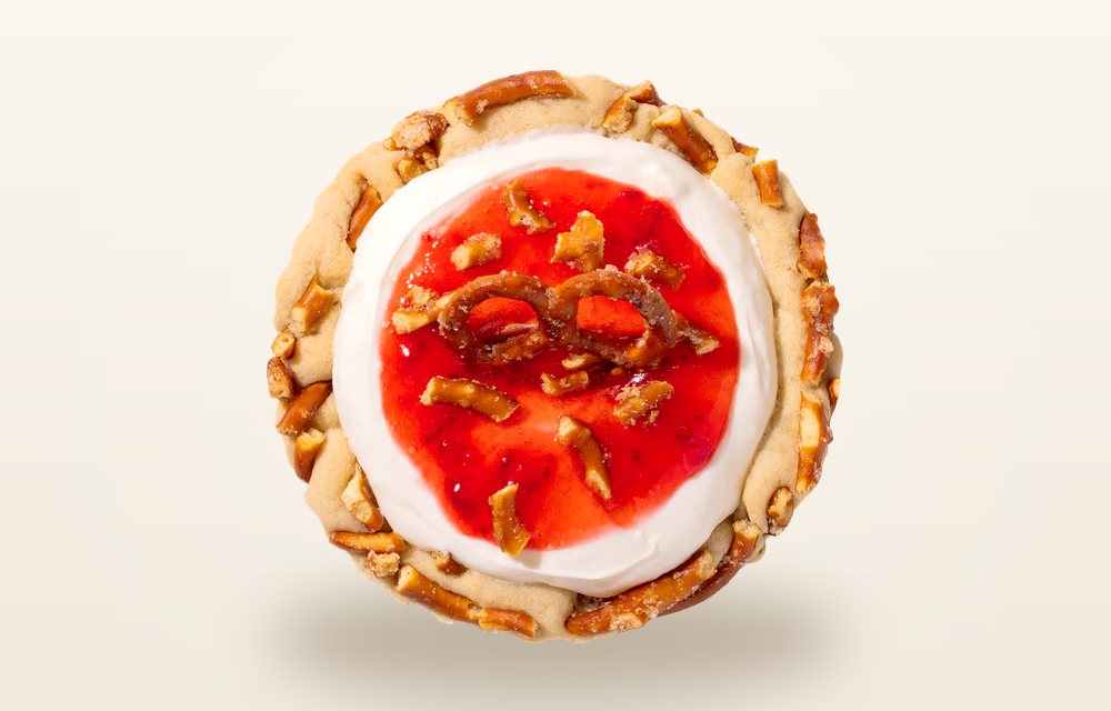 Overhead view of a Crumbl Strawberry Pretzel Pie cookie, a pretzel crust topped with white filling and chopped strawberries