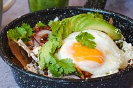 A bowl of white rice topped with a fried egg, sliced avocado and black beans