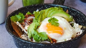 A bowl of white rice topped with a fried egg, sliced avocado and black beans