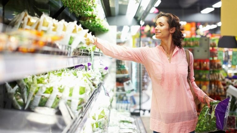 A woman choosing bagged greens in a produce aisle