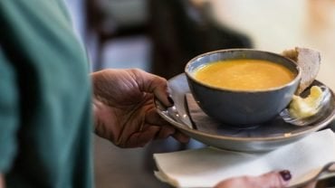 A bowl of creamy soup with bread and butter carried to a cafe table.