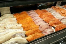 Rows of white fish and salmon fillets laid out in a lit seafood display case