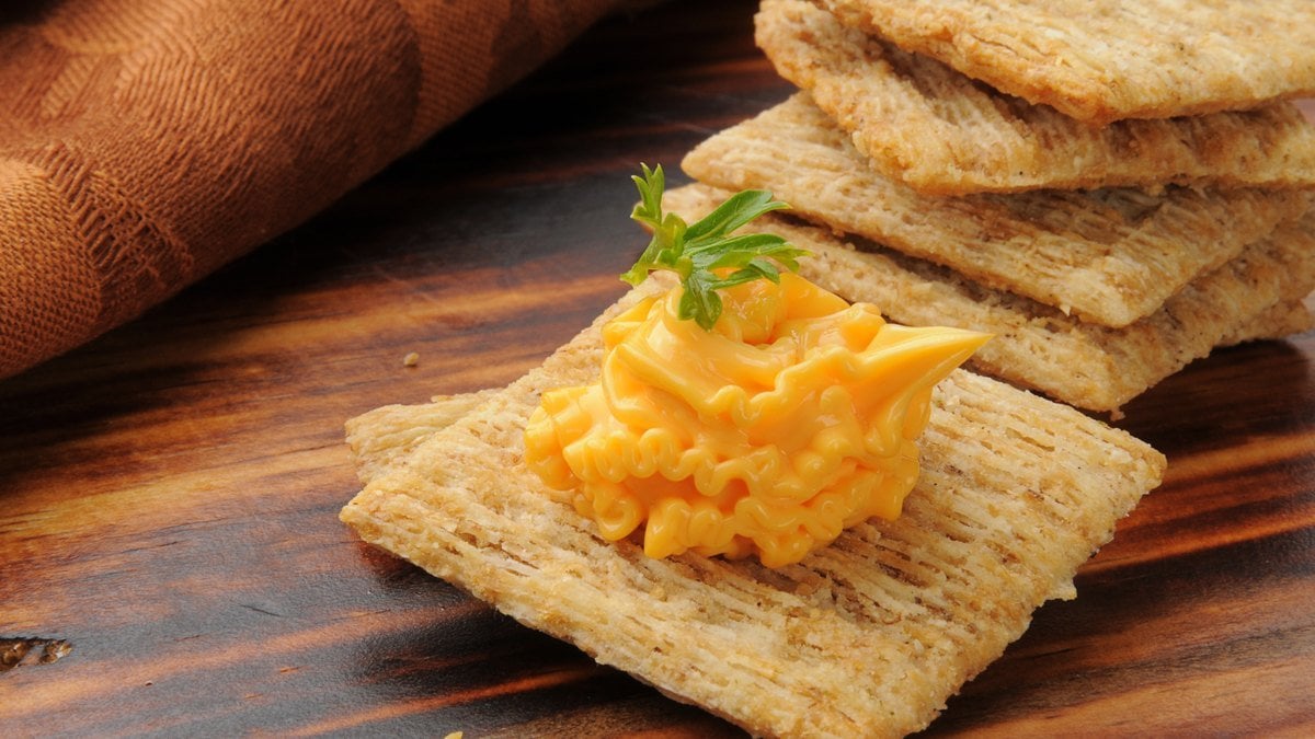 A ridged swirl of orange spray cheese piped onto a woven wheat cracker