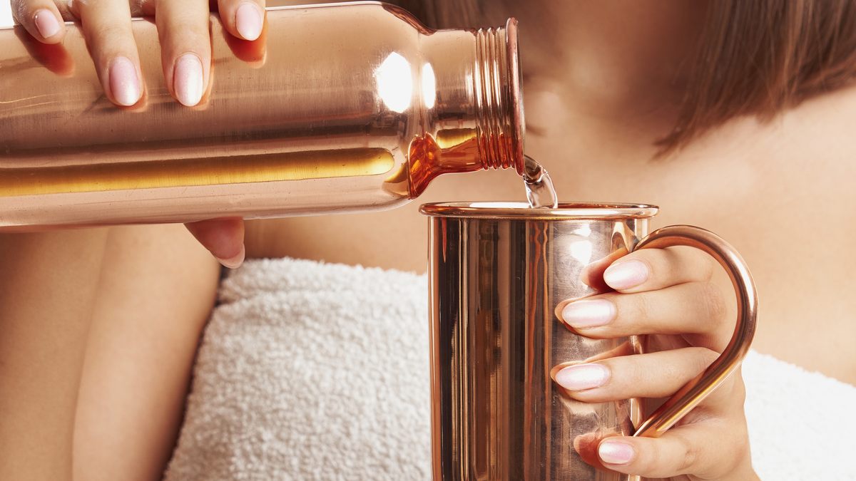Water being poured from a copper bottle into a copper mug