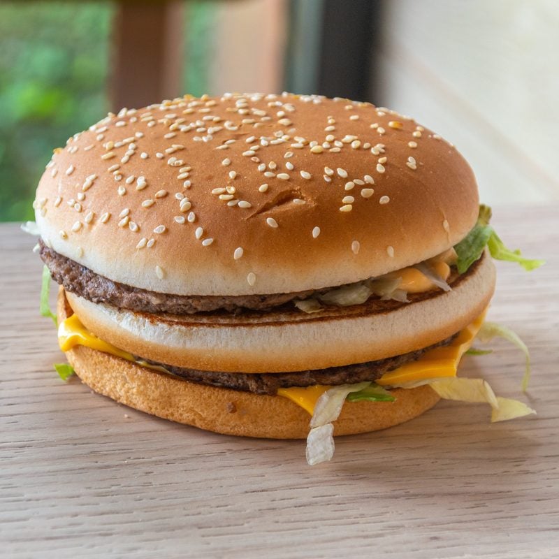 A Big Mac on a wooden table, its three-part sesame bun and two patties visible from the side