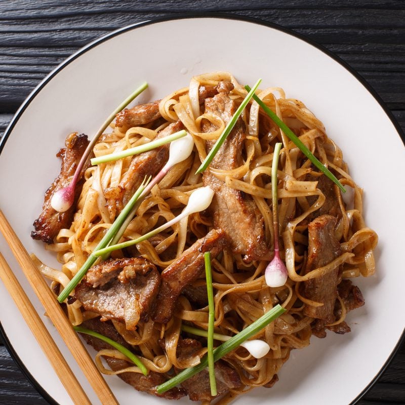 A plate of chow fun, wide flat rice noodles with sliced beef and scallions, seen from above
