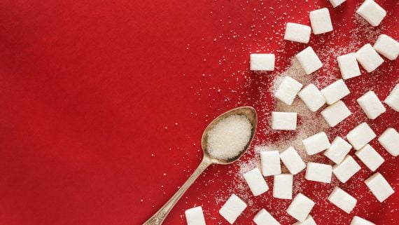 Sugar cubes and a spoonful of sugar on a red surface