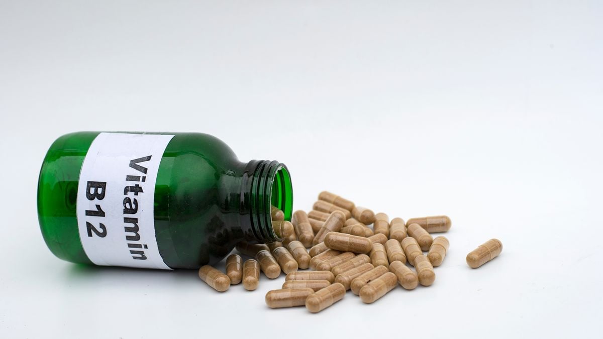 Green glass bottle labeled Vitamin B12 with capsules spilling out