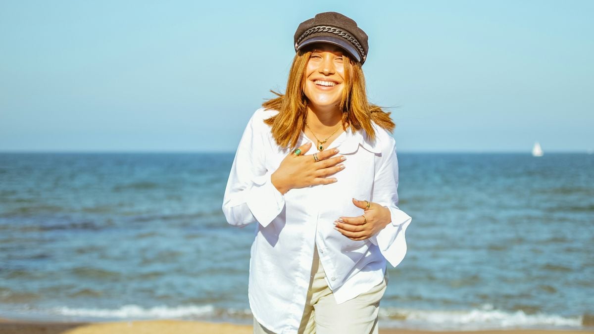 Woman in a white shirt and cap laughing on a sunny beach